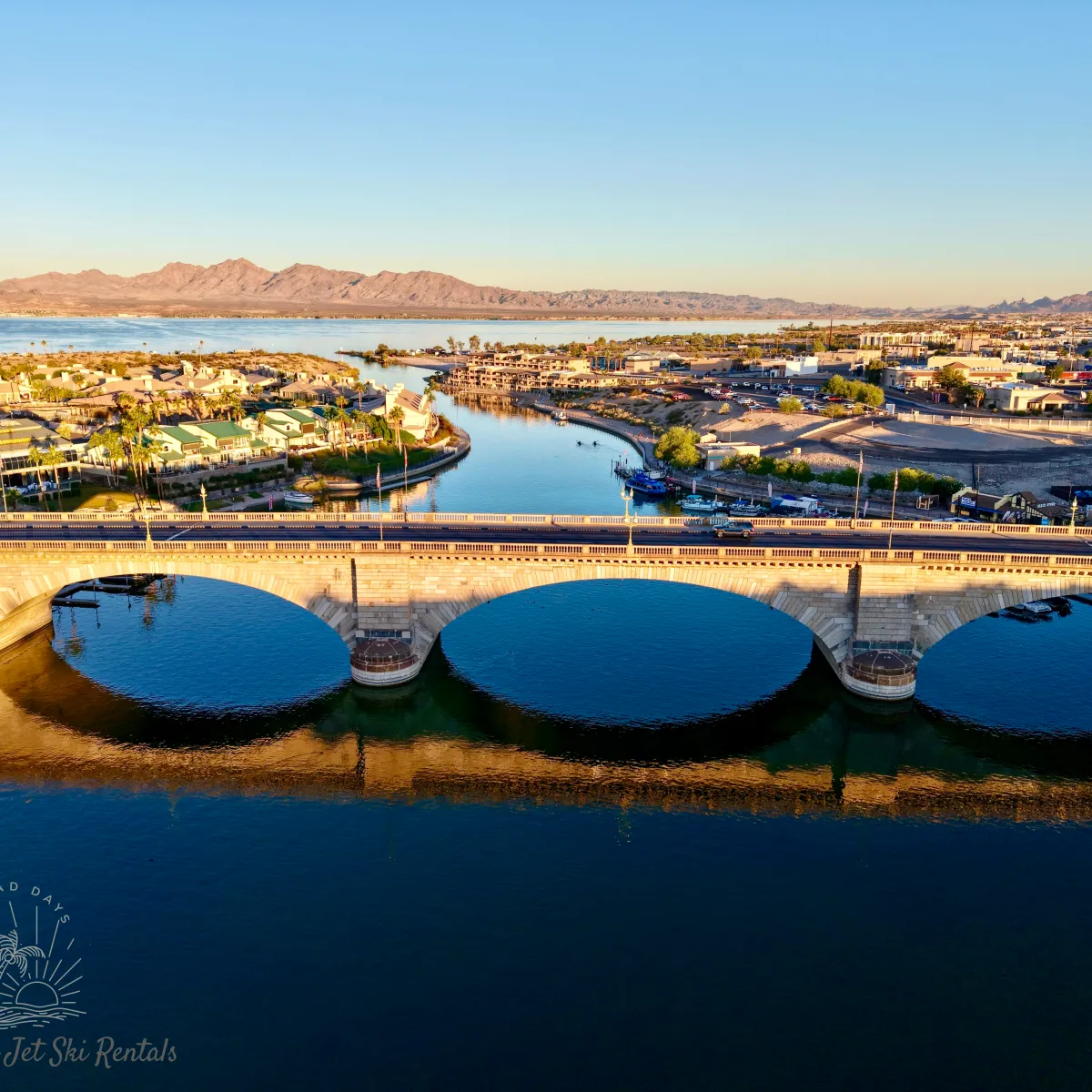 Aerial view of a stone bridge over a river connecting two landscapes with houses and a mountain in the background.
