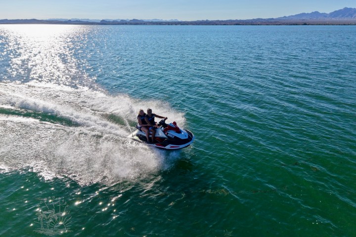 Two people riding a jet ski on a large lake with distant mountains.