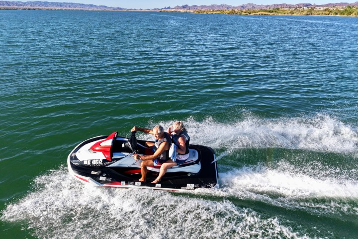 Couple riding a jet ski on a lake with distant mountains.