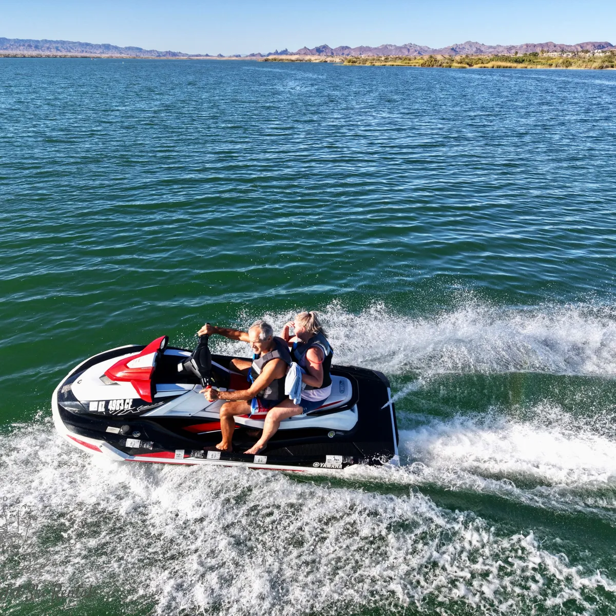 Couple riding a jet ski on a lake with distant mountains.
