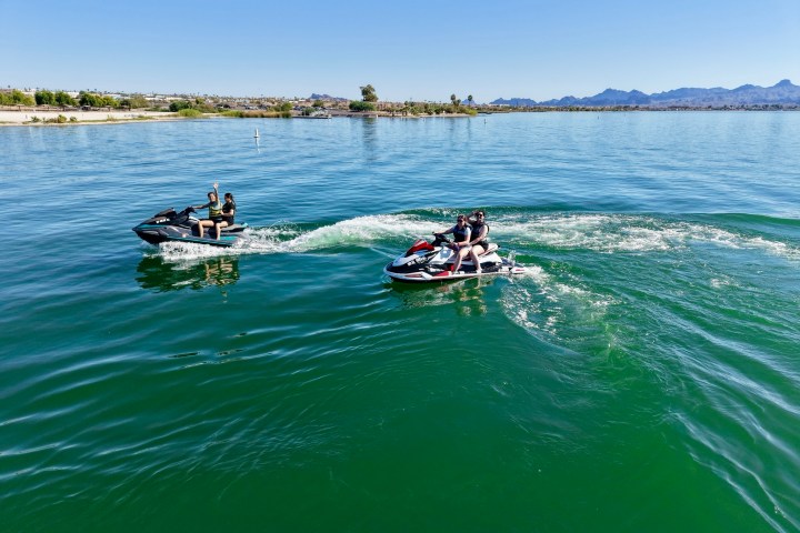 Two people on jet skis riding in a lake under a clear blue sky.