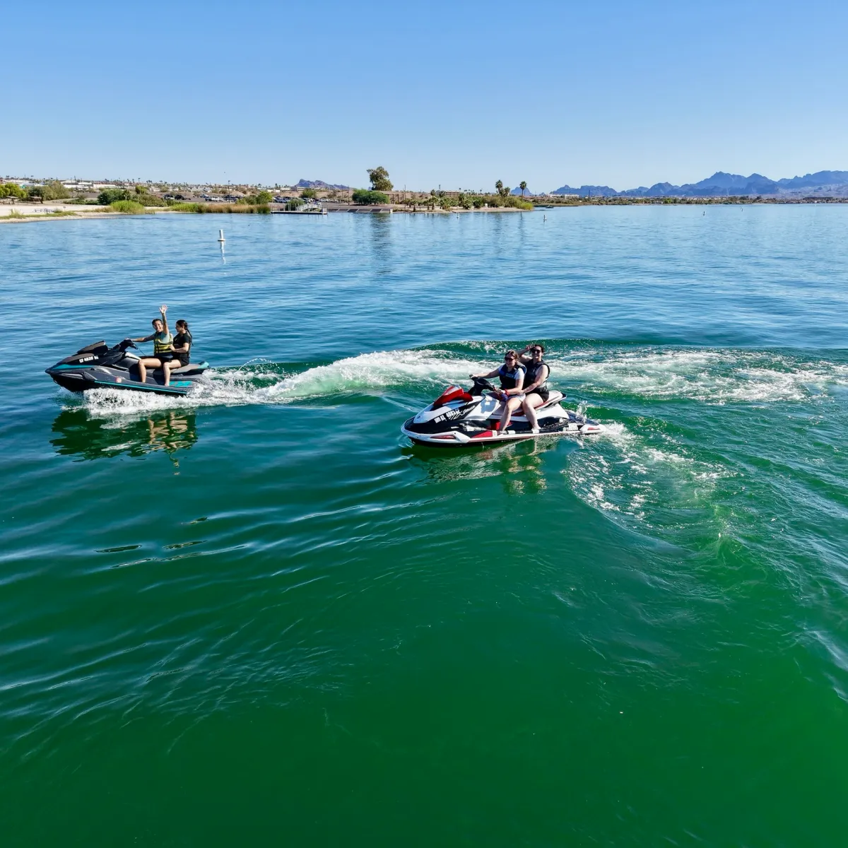 Two people on jet skis riding in a lake under a clear blue sky.